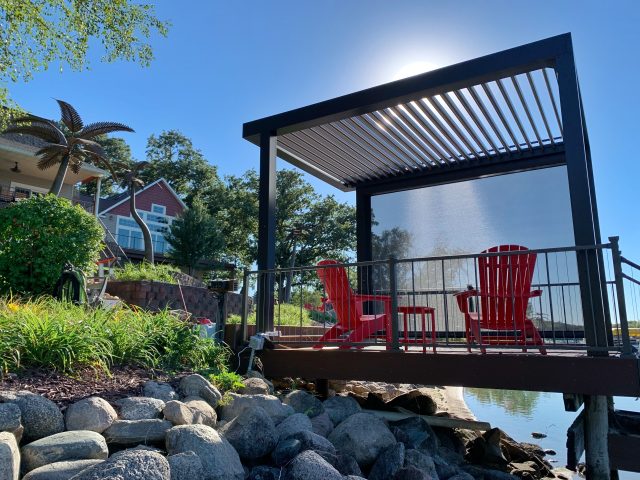 A deck with chairs and a pergola over the water.