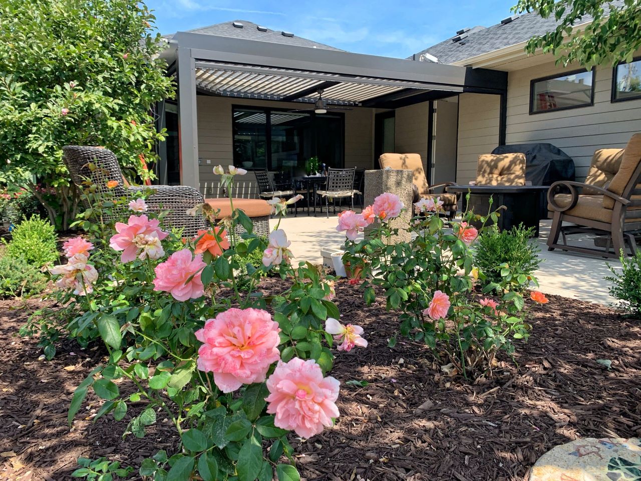 A patio with pink flowers and a large lawn.